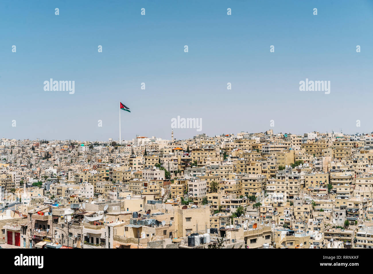 Jordanian flag flying over sunny city buildings, Amman, Jordan Stock Photo