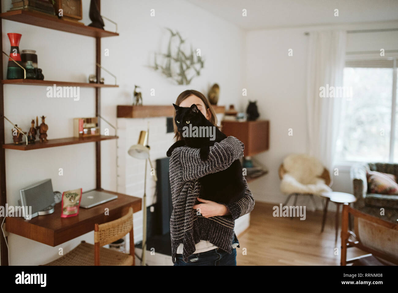 Girl holding black cat in living room Stock Photo