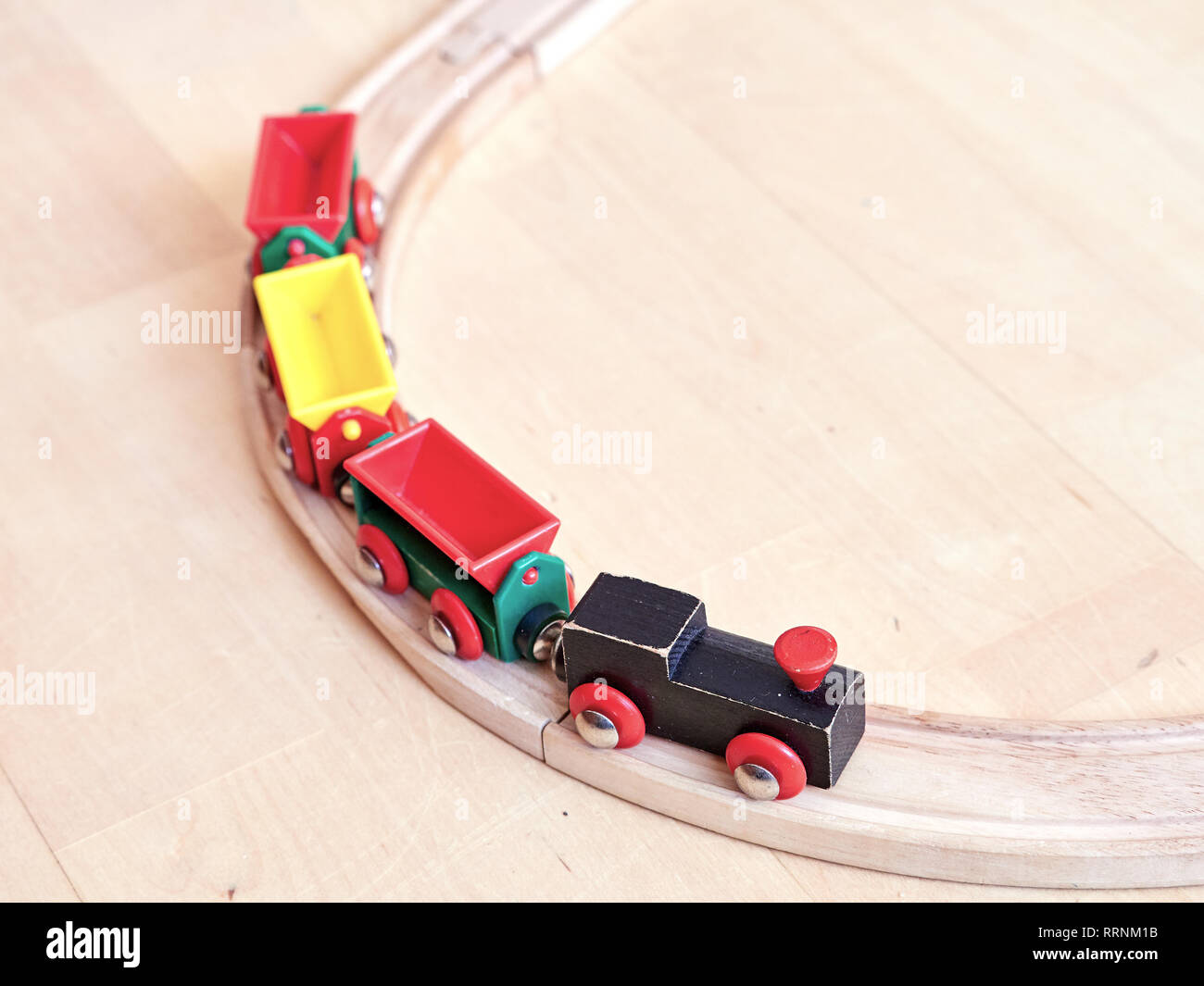 Wooden toy train running on miniature railroad. The black engine pulling colorful cars on the floor. Educational toys for children in preschool and ki Stock Photo
