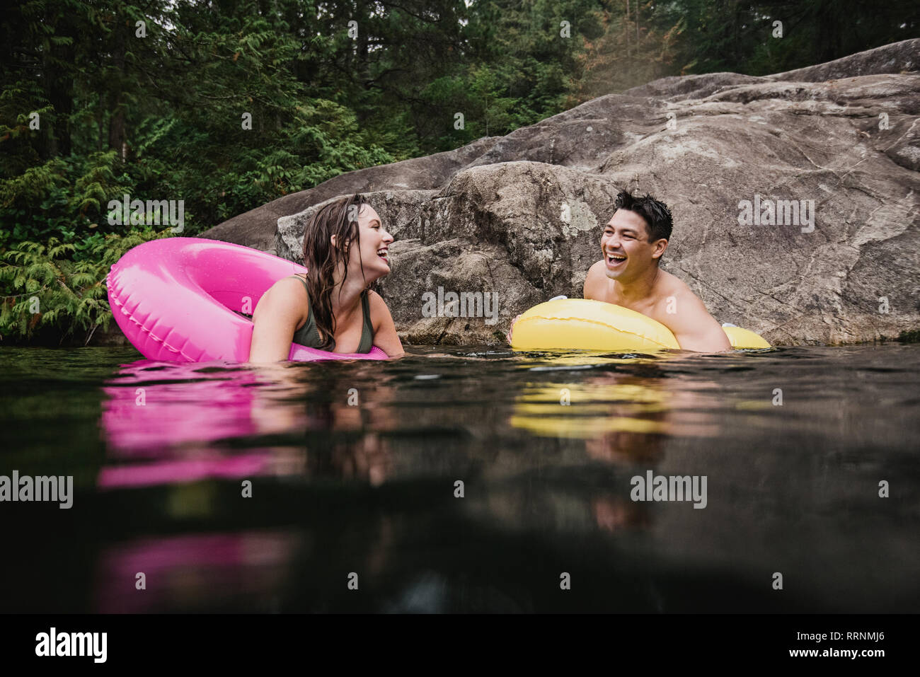 Happy young couple floating in inflatable rings on lake Stock Photo