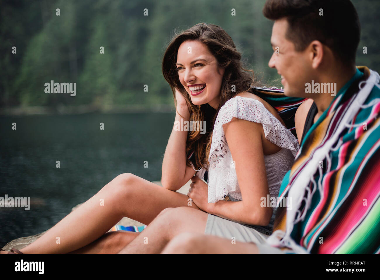Happy, carefree young couple wrapped in a blanket at lakeside Stock Photo