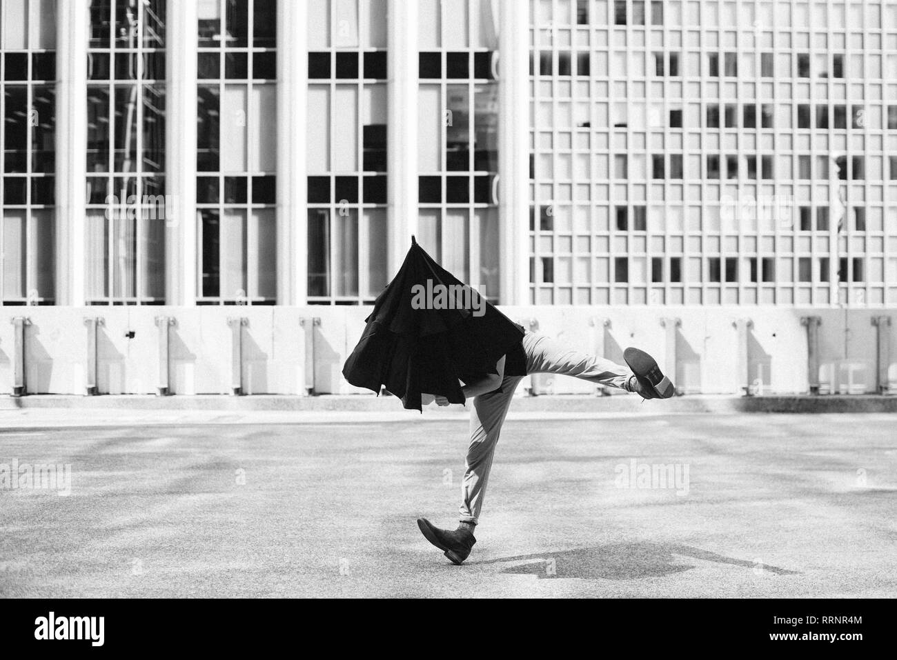 Man dancing with umbrella on head outside urban buildings Stock Photo