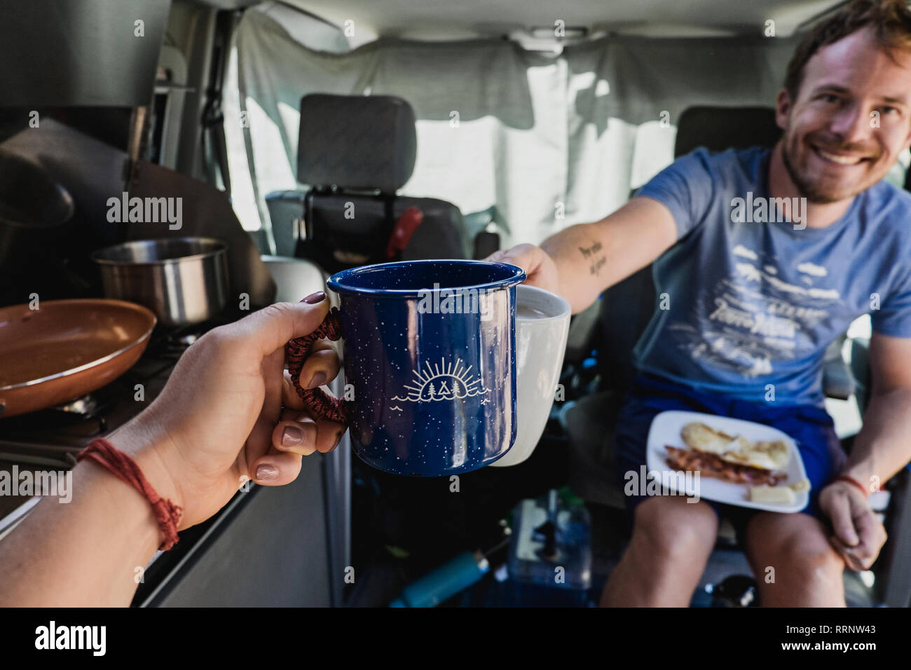Personal perspective couple toasting coffee cups in camper van Stock Photo