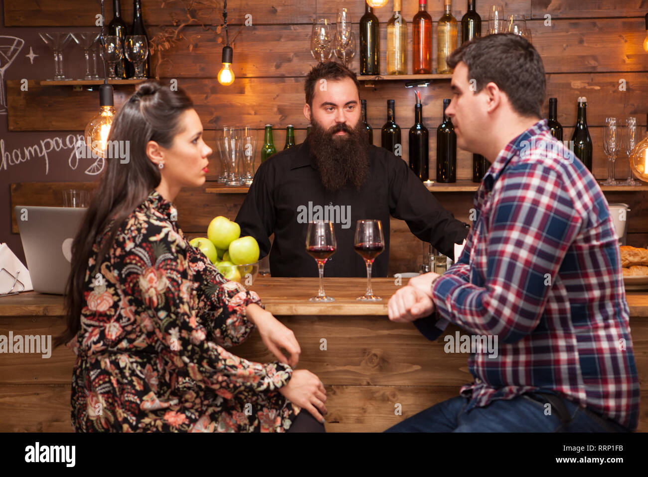 Young barman standing at bar counter talking with girl and her