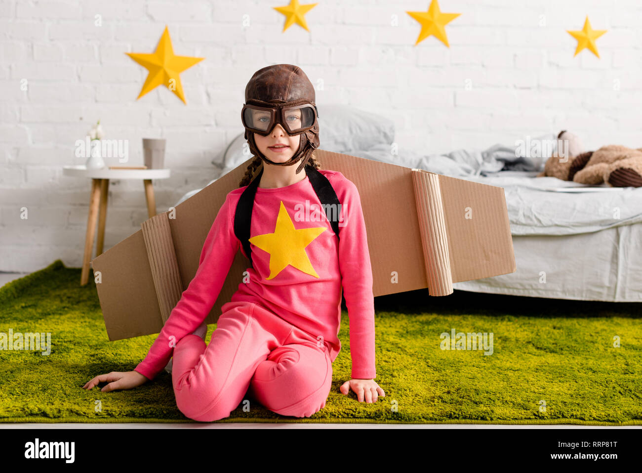 Curious kid in goggles and flight helmet sitting on green carpet Stock Photo