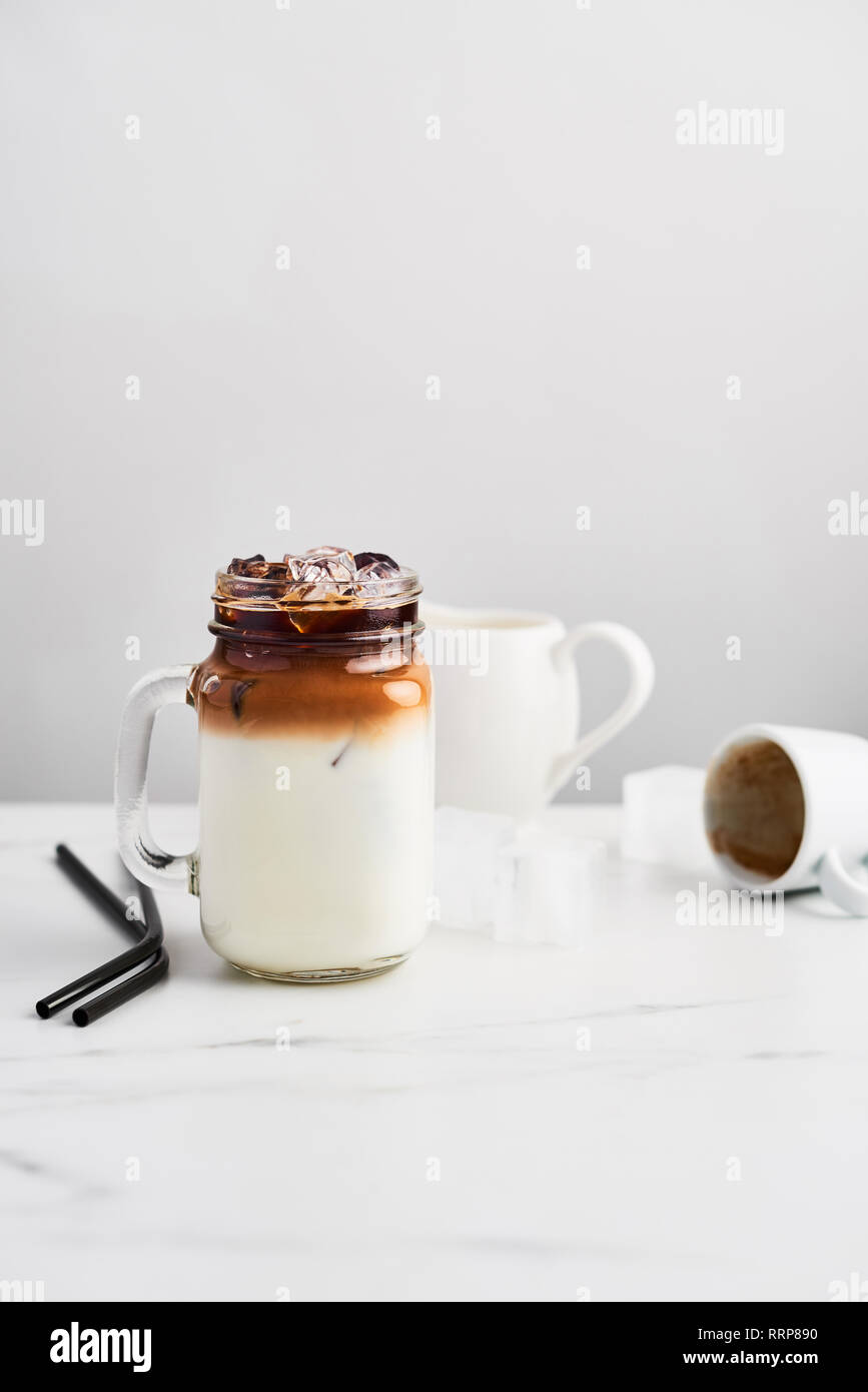 Ice coffee with milk in mason jar and black metal drinking straws on white marble table over white background. Copy space for text. Stock Photo