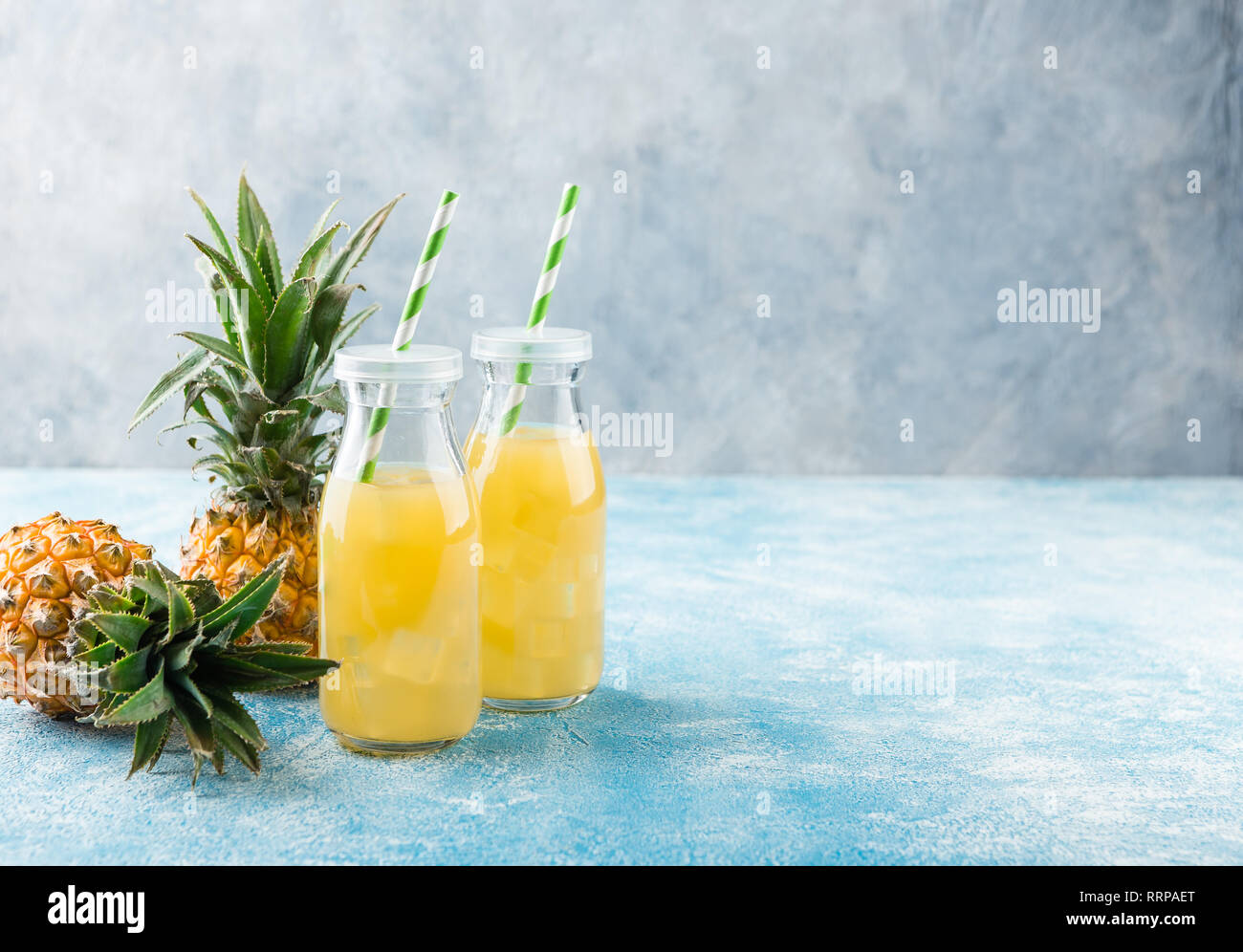 Pineapple cocktail or juice in two glass bottles with straws with ice and two mini pineapples on a blue background Stock Photo