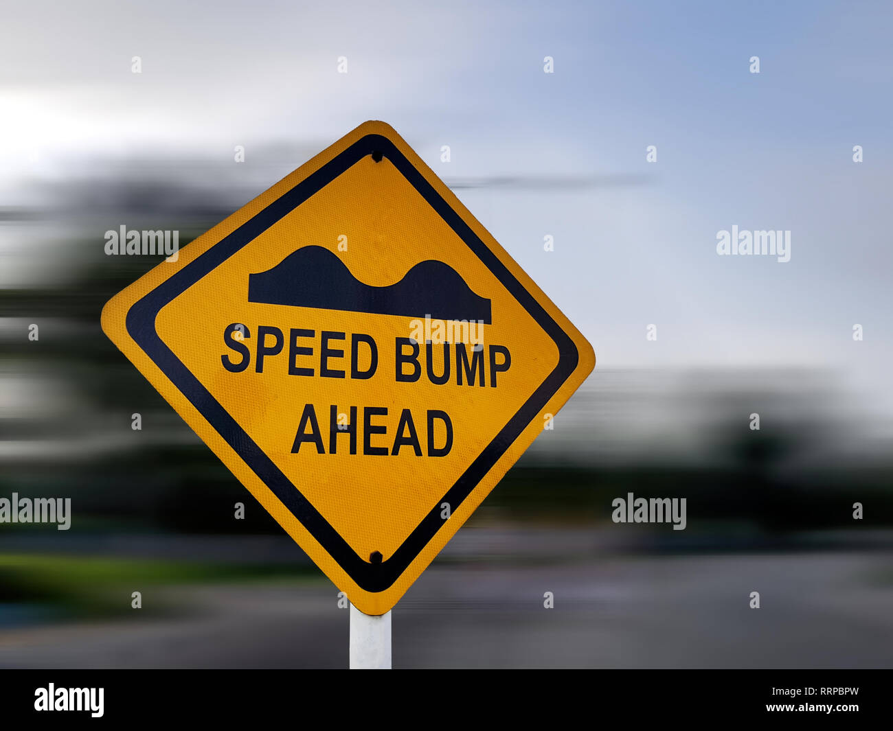 Speed Bump Sign - Yellow Road Traffic Warning Sign, on a Speeding Blurred Background Stock Photo
