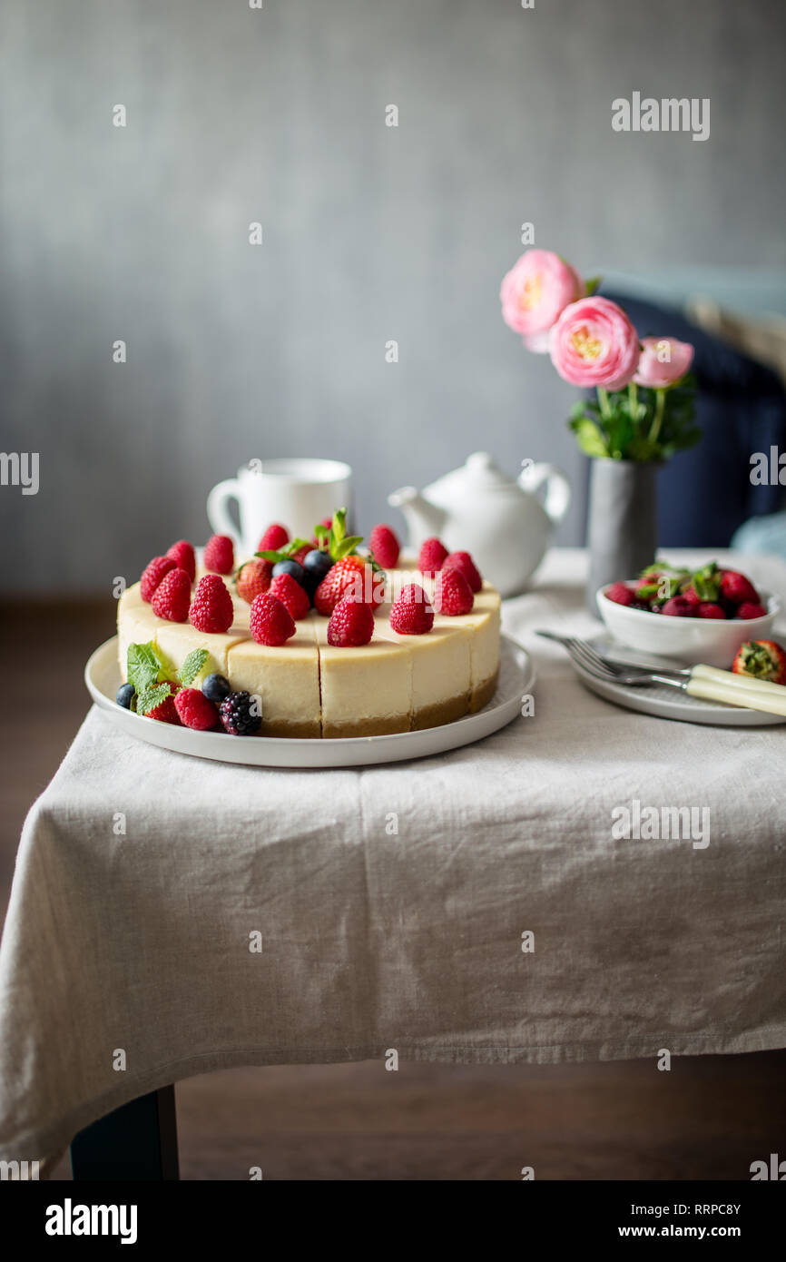 New York cheesecake on table in living room, fork, knife, vase with flowers, teapot and cup near. Concept of healthy live, view of sweet food Stock Photo