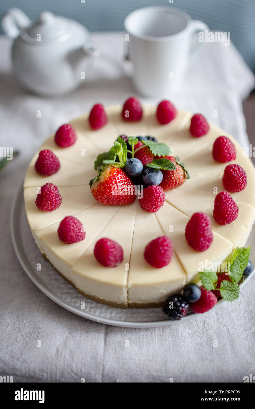 Close up fresh berry cheesecake on gray plate at table with cup and teapot, food photography, recipe idea for magazine, concept of sweet holiday food Stock Photo