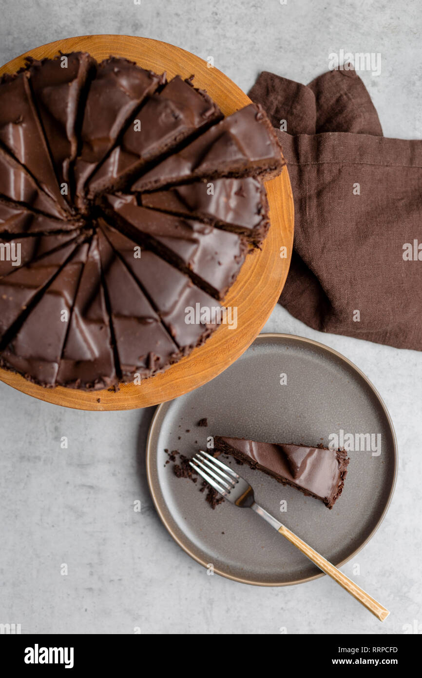 Sliced tasty chocolate cake on gray plate and on wooden stand, brown napkin near, on gray background. Top view vertical concept of sweet food. Stock Photo