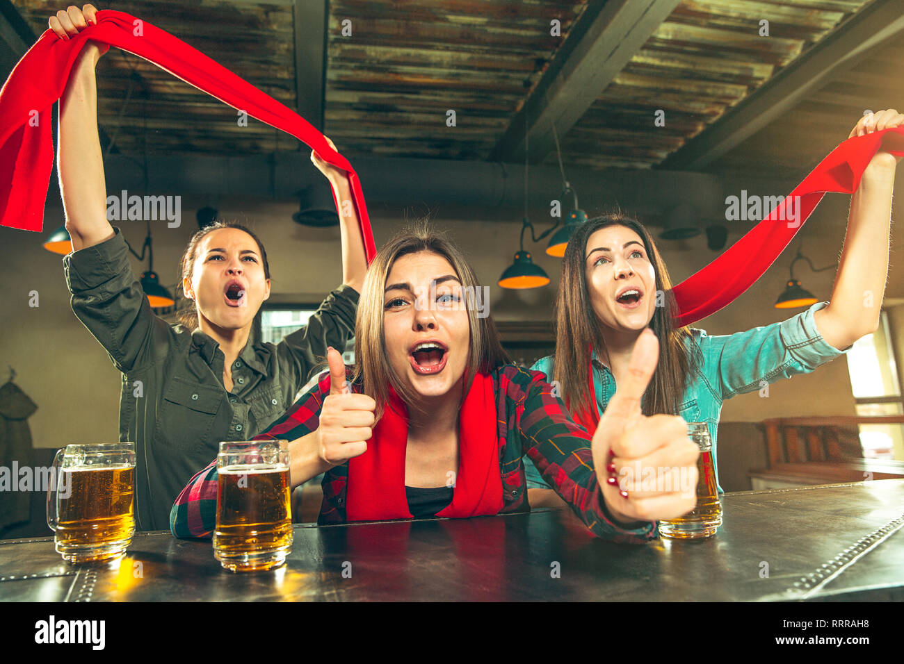 Sport, people, leisure, friendship, entertainment concept - happy female football fans or good young friends drinking beer, celebrating victory at bar or pub. Human positive emotions concept Stock Photo