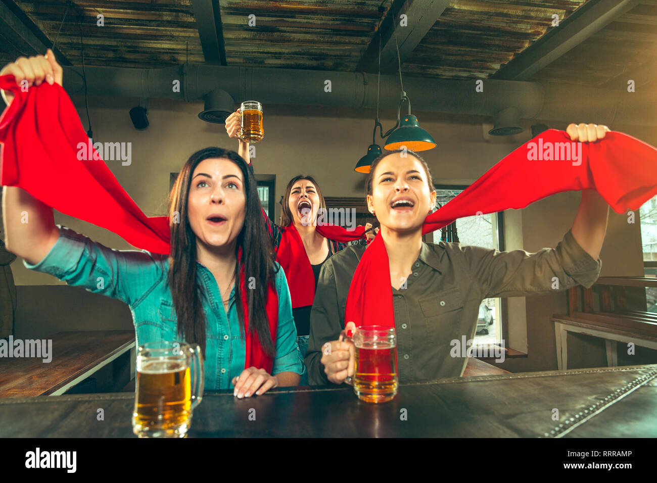 Sport, people, leisure, friendship, entertainment concept - happy female football fans or good young friends drinking beer, celebrating victory at bar or pub. Human positive emotions concept Stock Photo