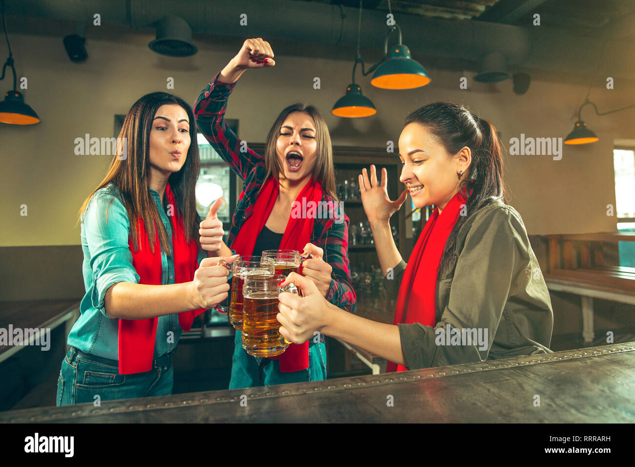 Sport, people, leisure, friendship, entertainment concept - happy female football fans or good young friends drinking beer, celebrating victory at bar or pub. Human positive emotions concept Stock Photo