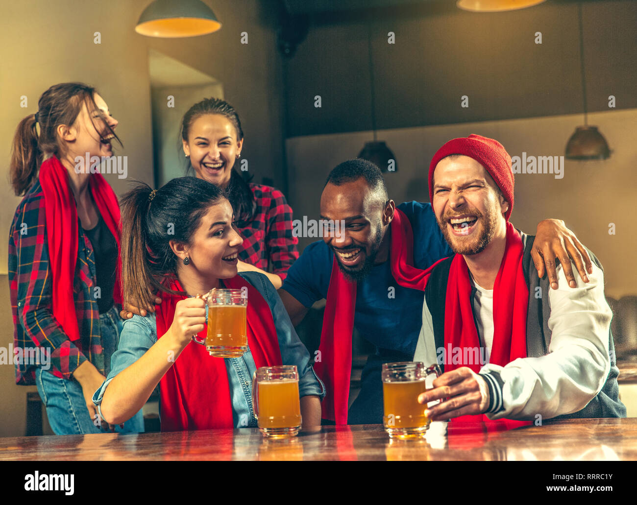 Sport, people, leisure, friendship, entertainment concept - happy male and female football fans or good young friends drinking beer, celebrating victory at bar or pub. Human positive emotions concept Stock Photo