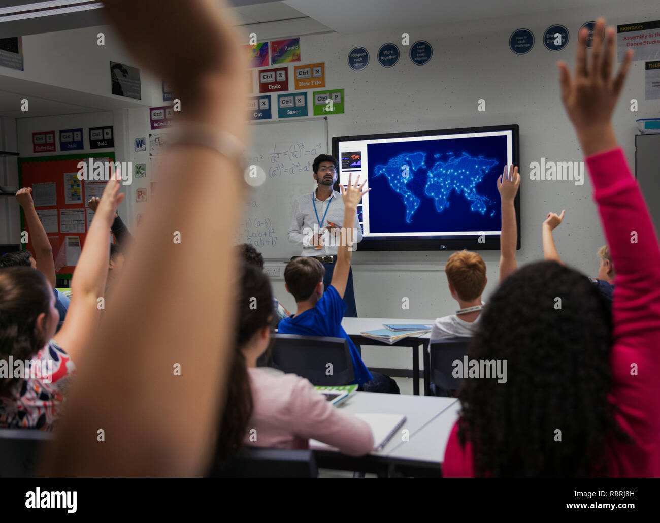 Junior high school students participating with hands raised in classroom Stock Photo