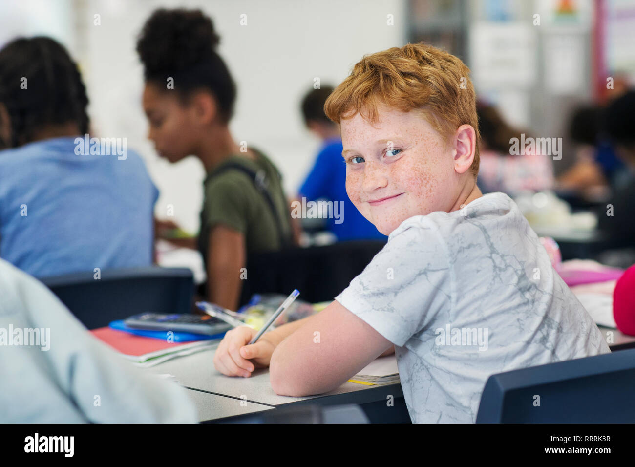 Portrait smiling, confident junior high school boy student studying at desk in classroom Stock Photo