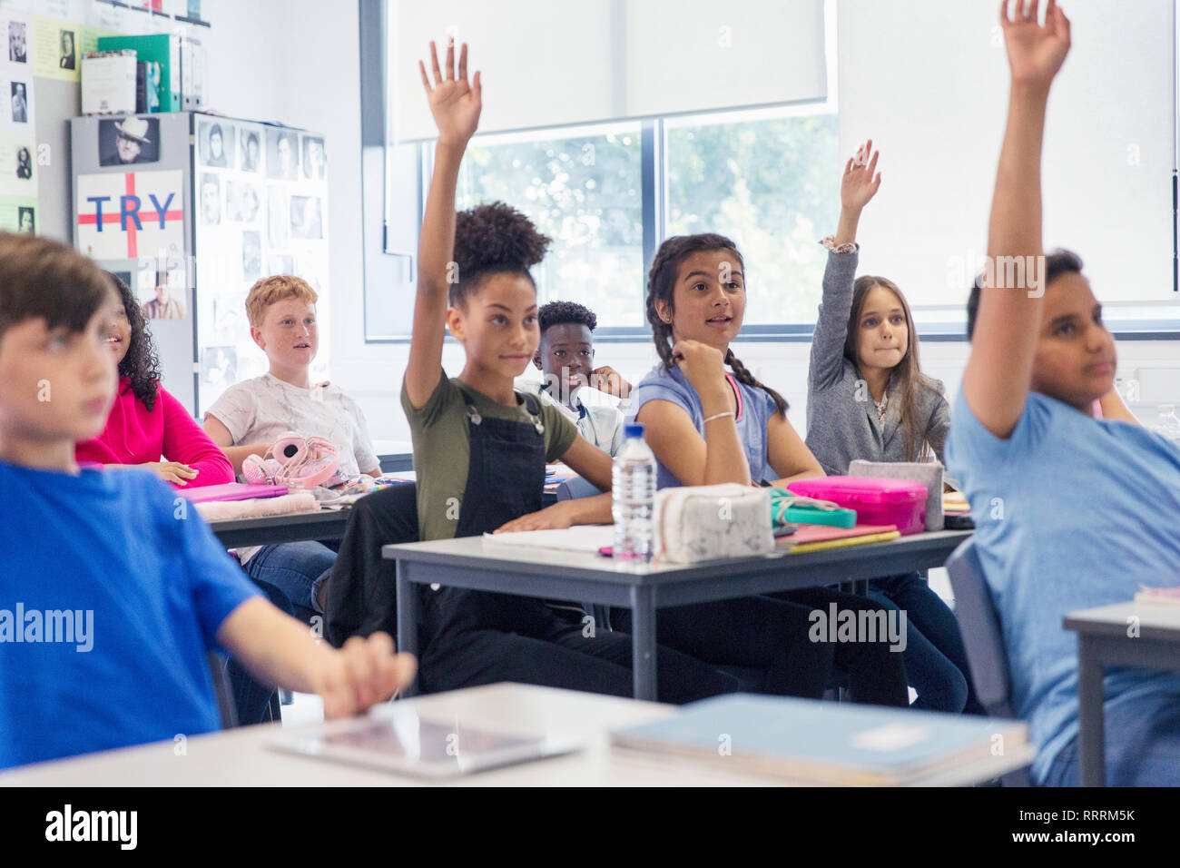 Junior high school students with hands raised in classroom Stock Photo