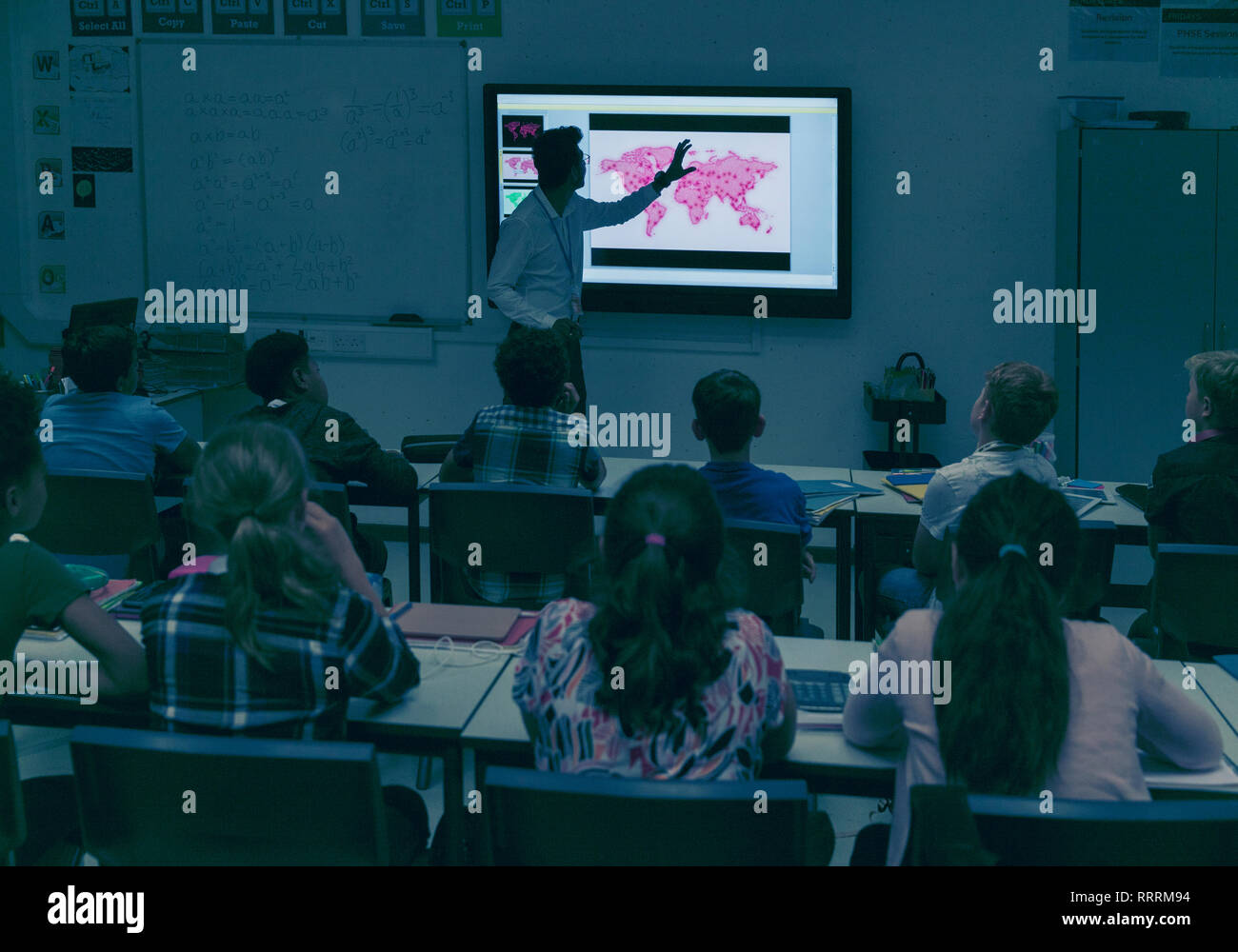 Students watching geography teacher at projection screen in dark classroom Stock Photo