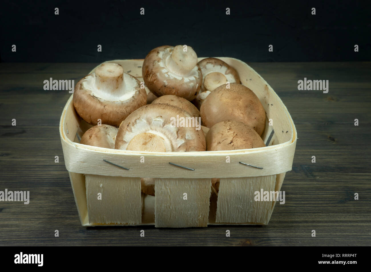 Fresh whole crimini (Baby Bella) mushrooms in the wooden basket on dark