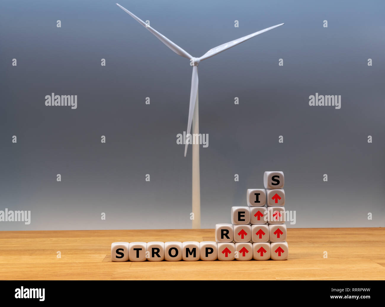 Symbol for increasing electricity rates. Dice form the German word 'Strompreis' ('electricity rate' in English) in front of a model wind turbine. Stock Photo