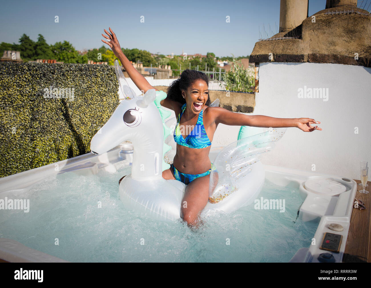 Playful, exuberant young woman in bikini sitting n inflatable pegasus in rooftop hot tub Stock Photo