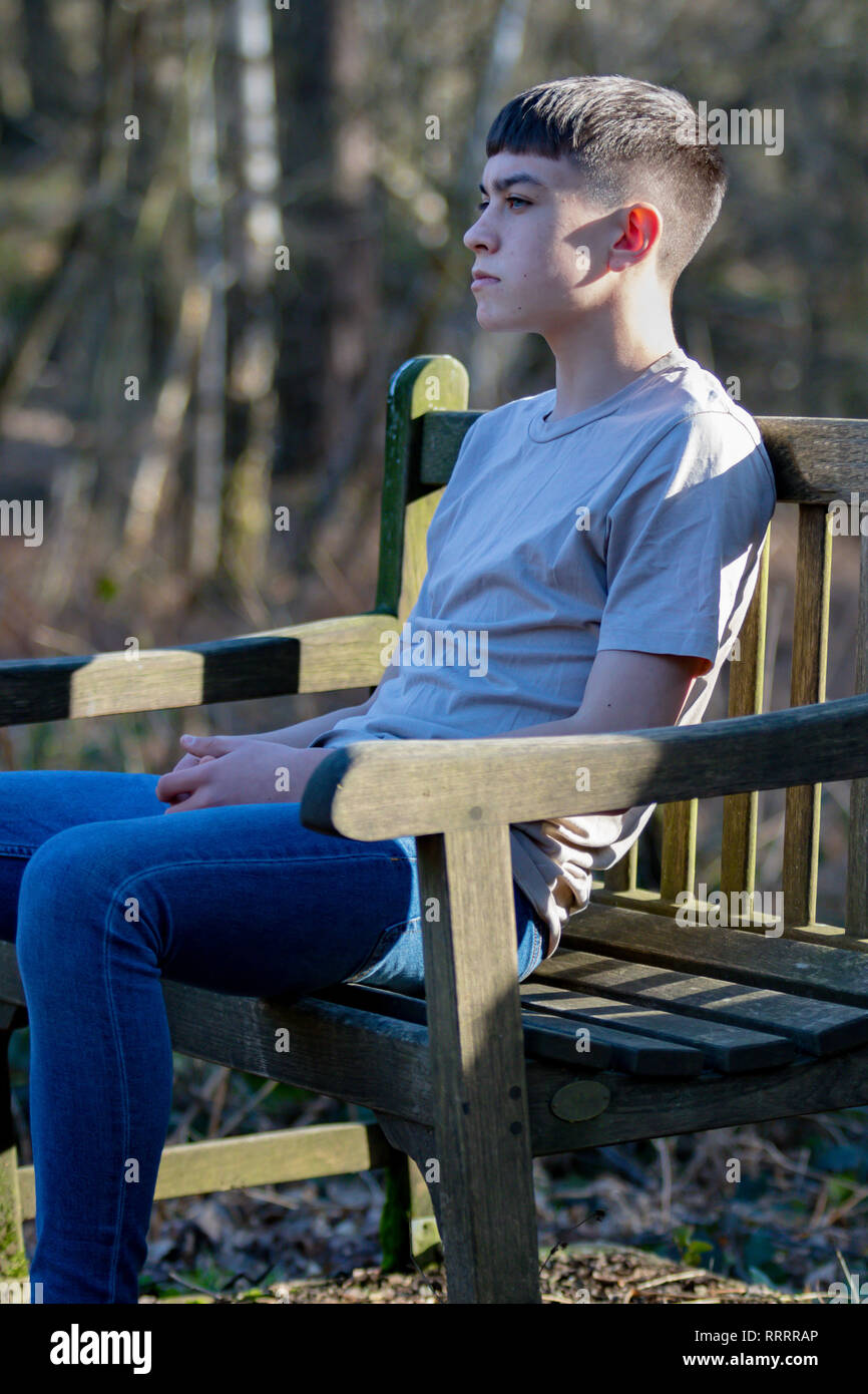 Portrait of a caucasian teenage boy sitting on a park bench on a warm ...
