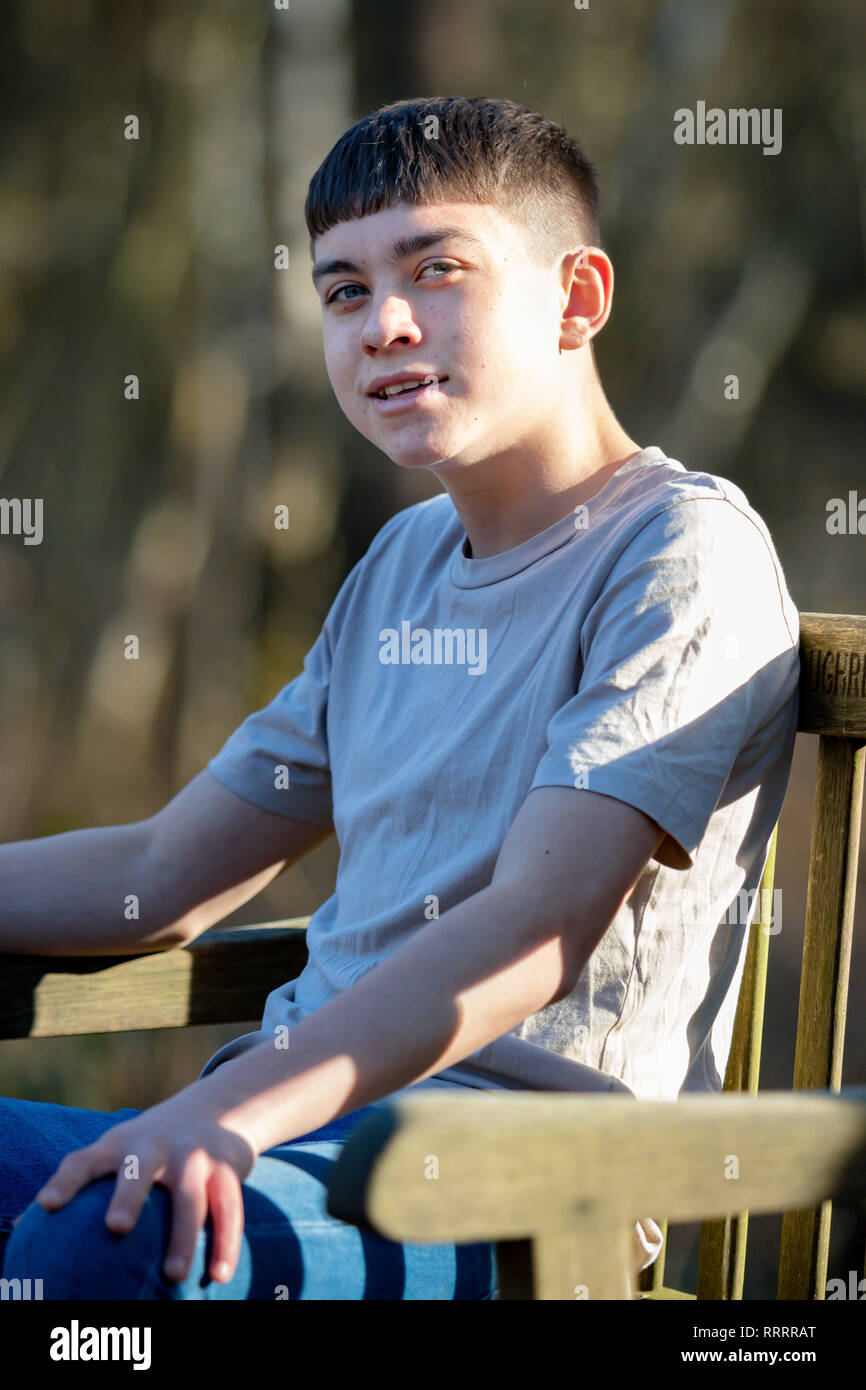 Portrait of a caucasian teenage boy sitting on a park bench on a warm ...