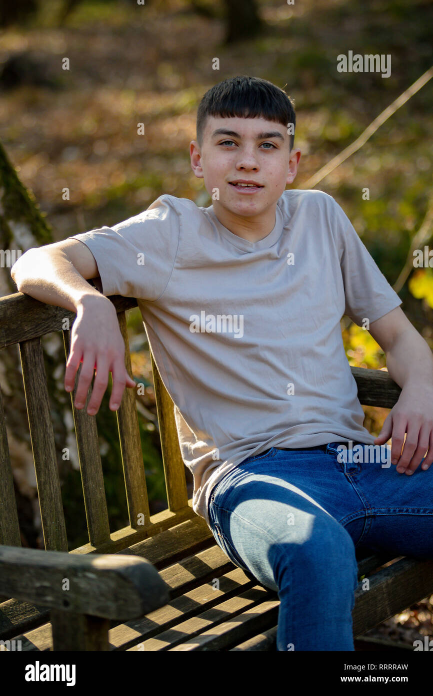 Portrait of a caucasian teenage boy sitting on a park bench on a warm ...