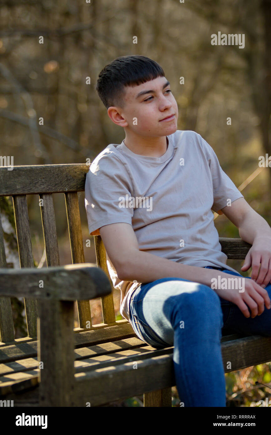 Portrait of a caucasian teenage boy sitting on a park bench on a warm ...