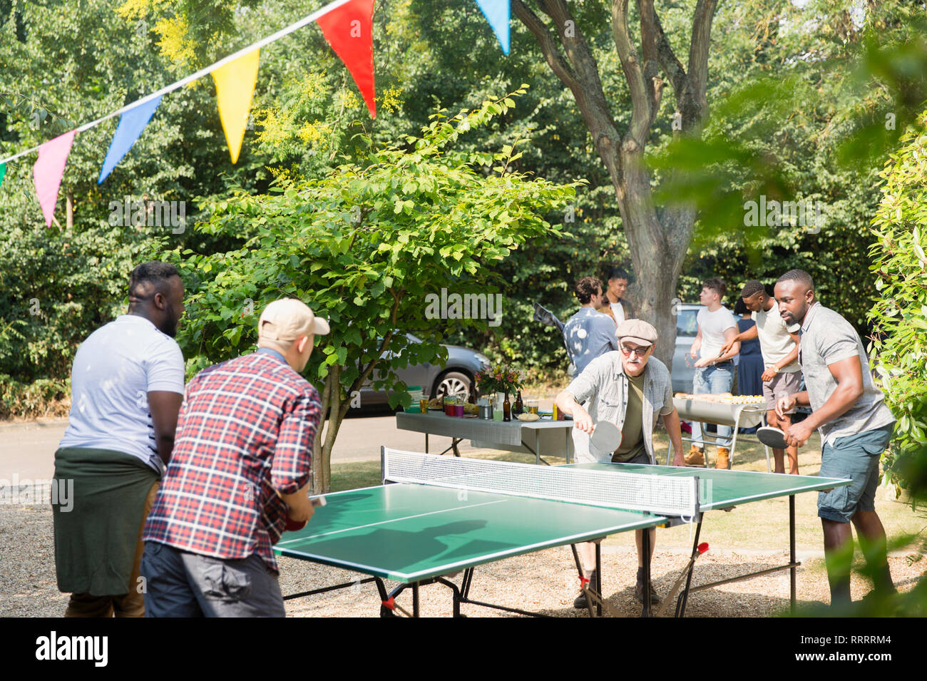 Male friends playing ping pong in sunny back yard Stock Photo