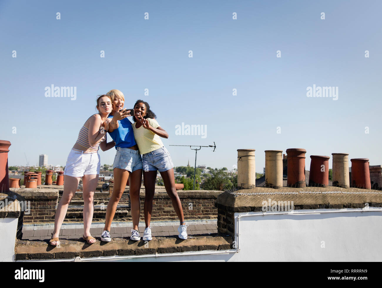 Young women friends taking selfie with camera phone on sunny rooftop Stock Photo