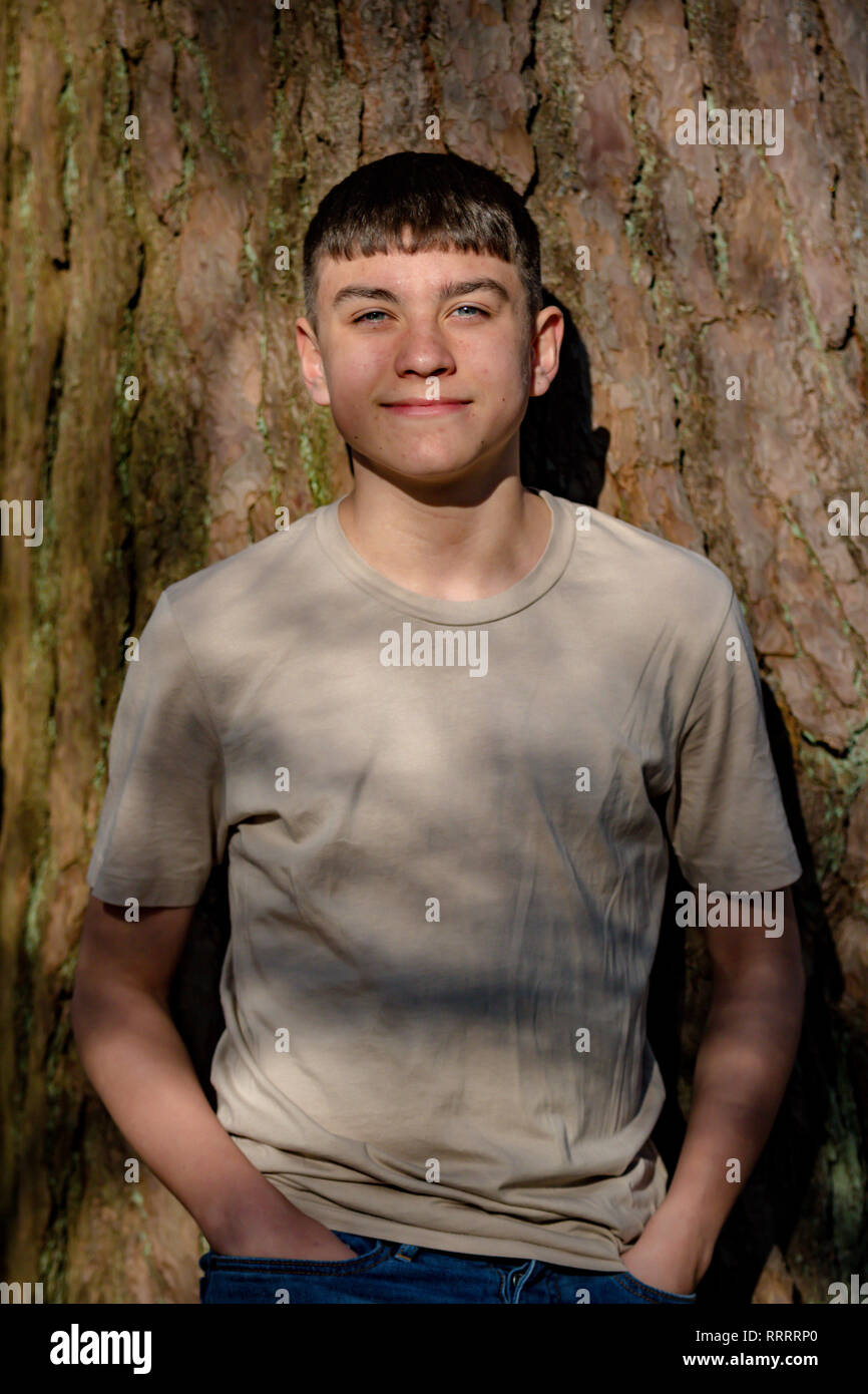 Portrait of a caucasian teenage boy leaning against a tree on a warm ...