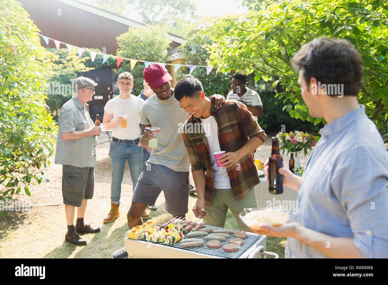 Male friends drinking beer and barbecuing in sunny summer backyard Stock Photo