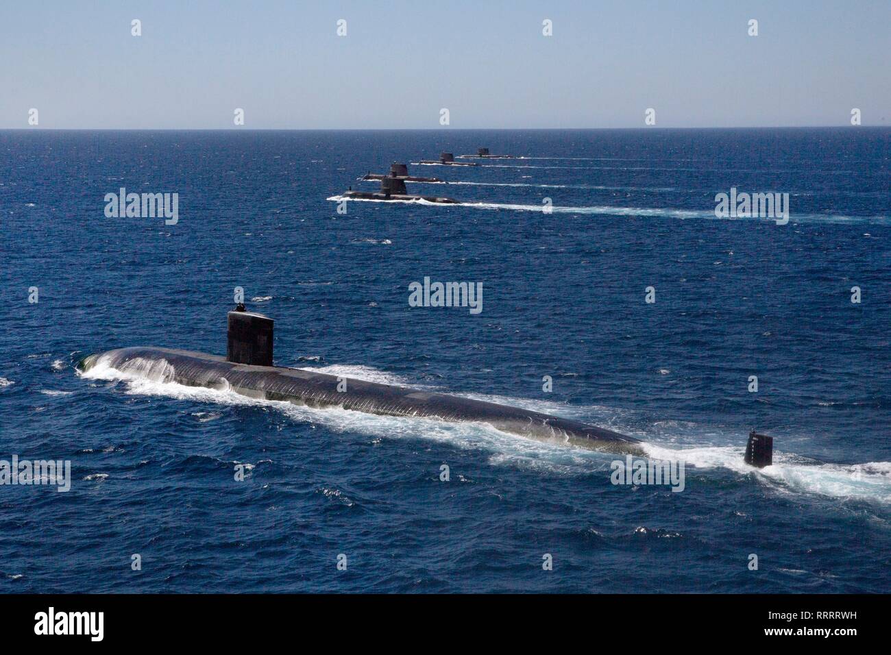 The U.S. Navy Los Angeles-class attack submarine USS Santa Fe sails in formation with Royal Australian Navy Collins class submarines HMAS Collins, HMAS Farncomb, HMAS Dechaineux and HMAS Sheean, as an Australian MH-60R Seahawk helicopter flies overhead in the West Australian exercise area February 18, 2019 off the coast of Fremantle, Australia. Stock Photo