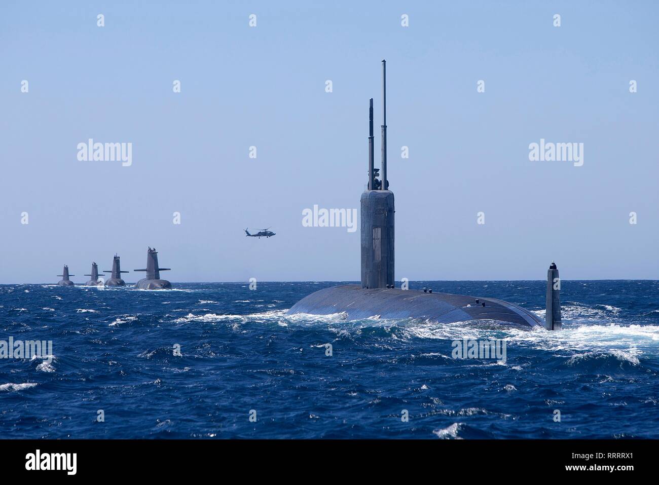 The U.S. Navy Los Angeles-class attack submarine USS Santa Fe sails in formation with Royal Australian Navy Collins class submarines HMAS Collins, HMAS Farncomb, HMAS Dechaineux and HMAS Sheean, as an Australian MH-60R Seahawk helicopter flies overhead in the West Australian exercise area February 18, 2019 off the coast of Fremantle, Australia. Stock Photo