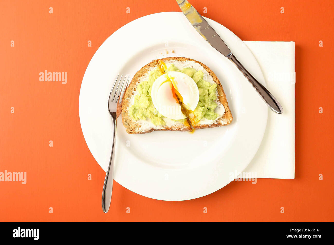 Eating avocado on toast with poached egg at a cafe.  Living coral colour table. Stock Photo