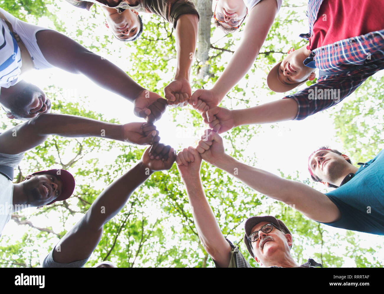 View from below mens group joining fists in circle, hiking under trees Stock Photo