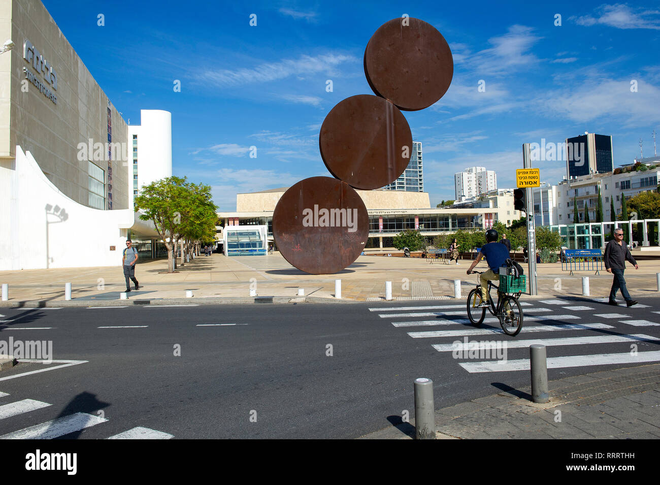 Pedestrians and cyclists in HaBima Square, Tel Aviv, Israel. In the middle, the Hitromemut (“elevation”) installation by artist Menashe Kadishman, Stock Photo