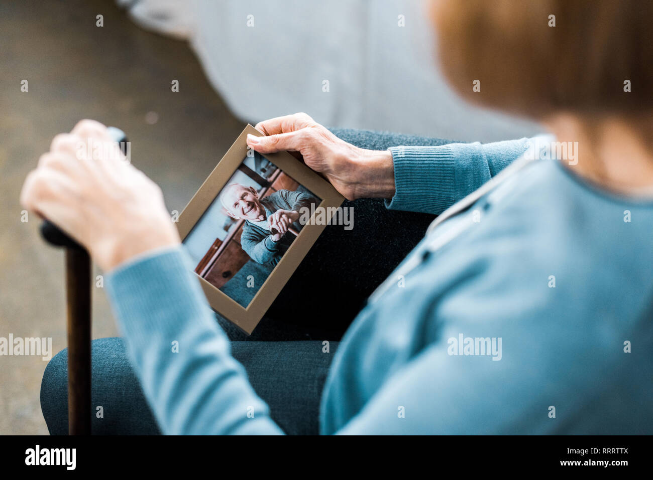 cropped view of senior woman sitting with walking stick and looking at frame with man on photograph Stock Photo