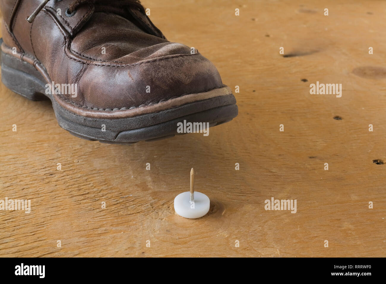 Closeup of an elevated shoe about to step on a jumbo thumbtack on a