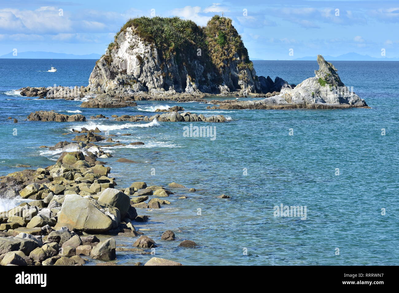 Horizontal view of rocks stretching from shore to rocky islet near harbor mouth in Mangawhai Heads. Stock Photo