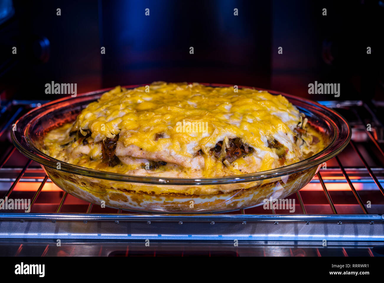 Nutritious organic healthy Layered meat pie with vegetables and mushrooms covered with grated cheese baked in a glass round baking tray in a desktop e Stock Photo