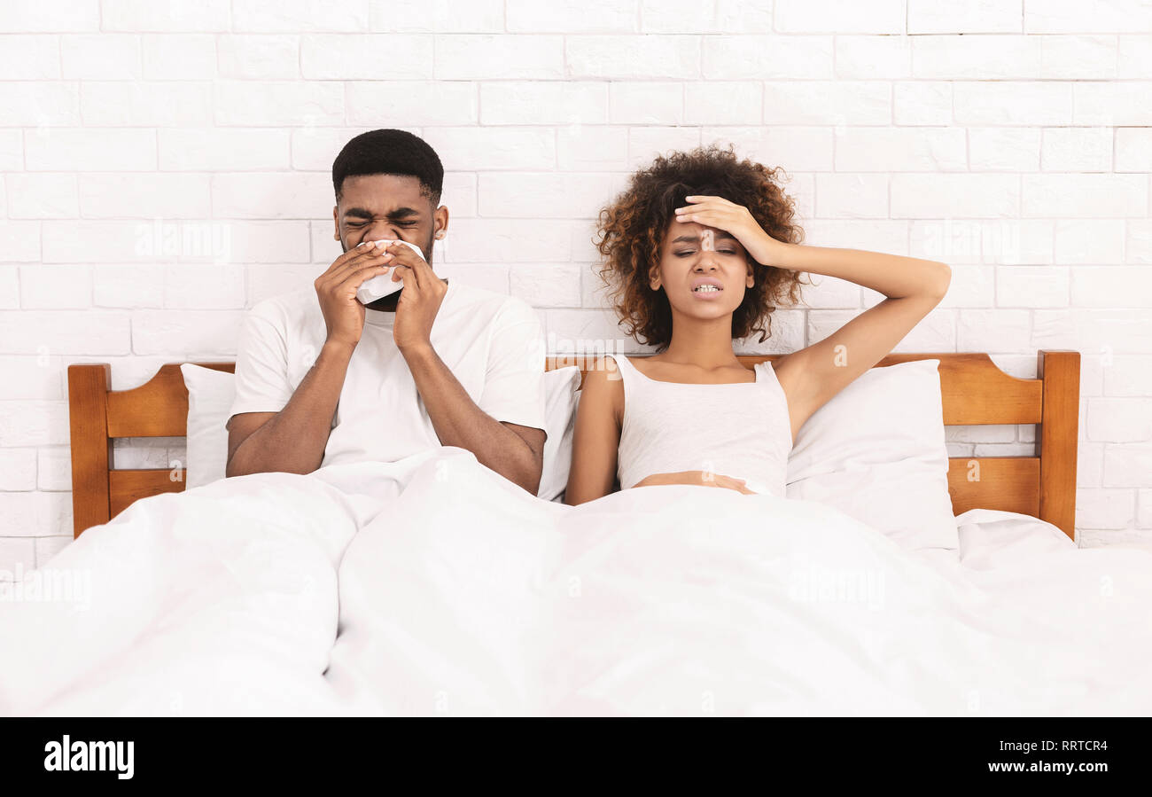 Sick african-american couple blowing noses in bed Stock Photo