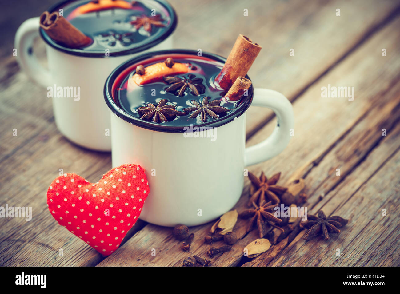 Mulled wine in mugs, red heart and spice on old wooden table. Retro styled. Stock Photo