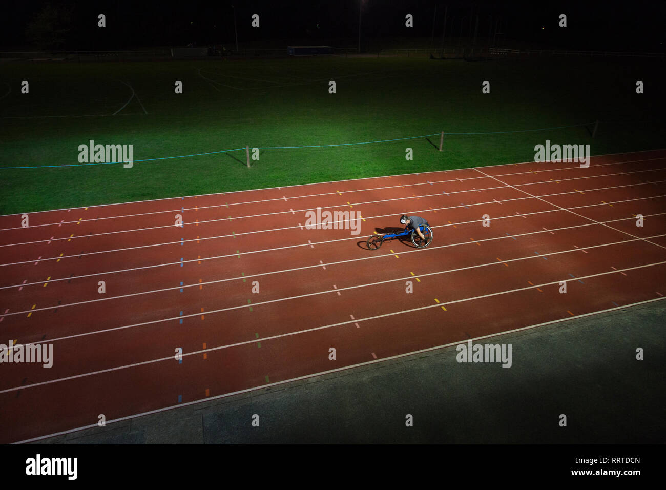 Paraplegic athlete speeding along sports track in wheelchair race at night Stock Photo