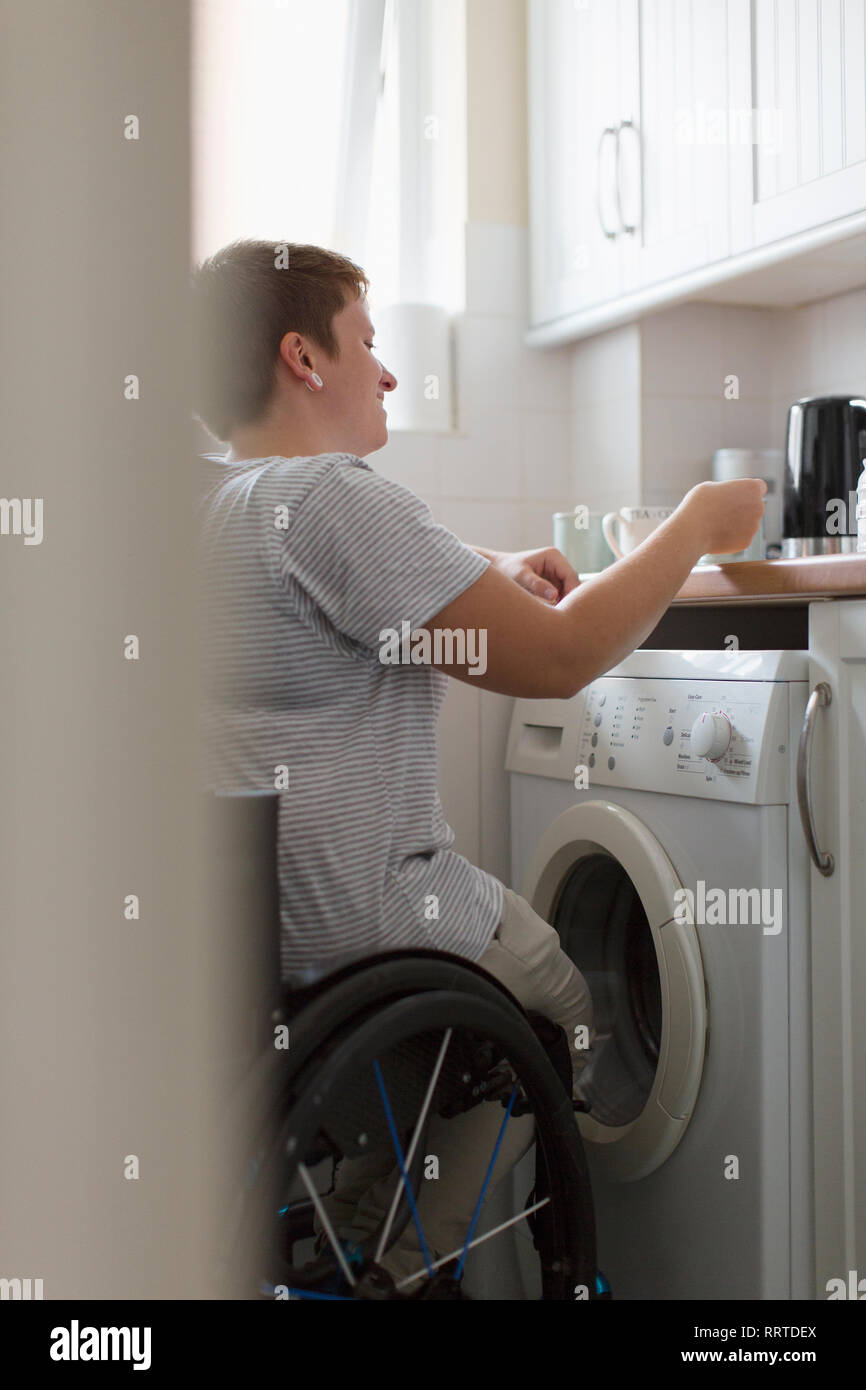 Young woman in wheelchair preparing tea in apartment kitchen Stock Photo