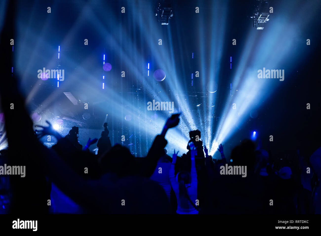 Silhouettes of a concert crowd and cameraman against the background of bright, colorful rays on the stage. Camera with the operator is on the high pla Stock Photo