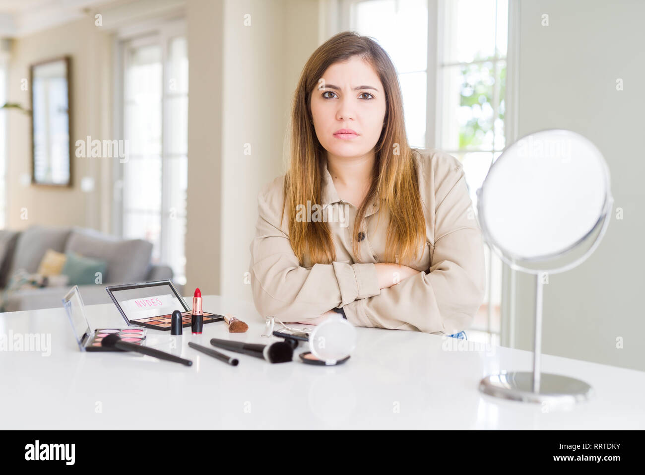 Beautiful young woman using make up cosmetics skeptic and nervous, disapproving expression on face with crossed arms. Negative person. Stock Photo