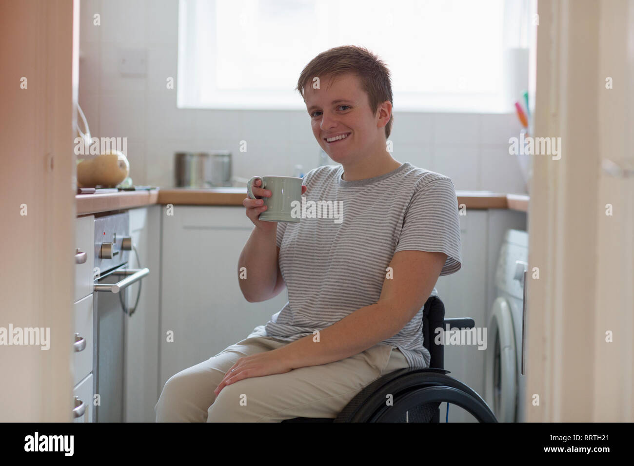 Portrait smiling, confident young woman in wheelchair drinking tea in apartment kitchen Stock Photo